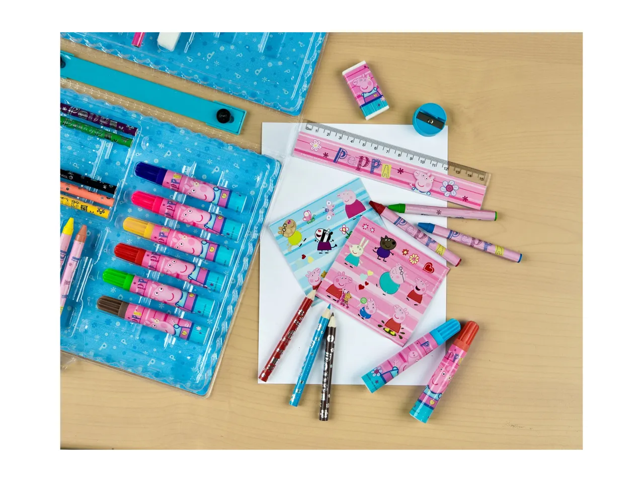 A teal art supply case with crayons, markers, and other stationery items is shown on a light wood surface.
