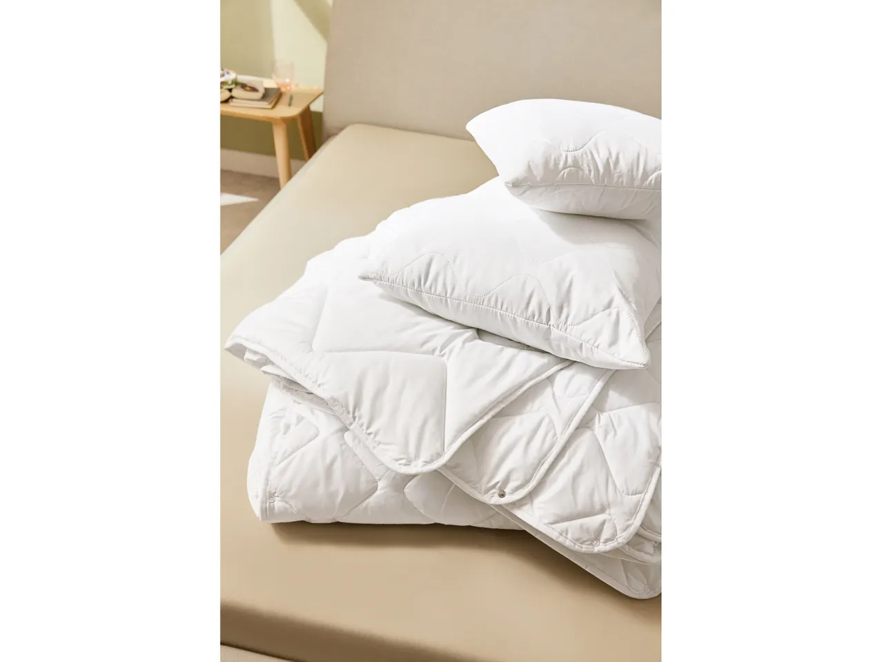Piumino e cuscini bianchi trapuntati piegati su un letto color crema.