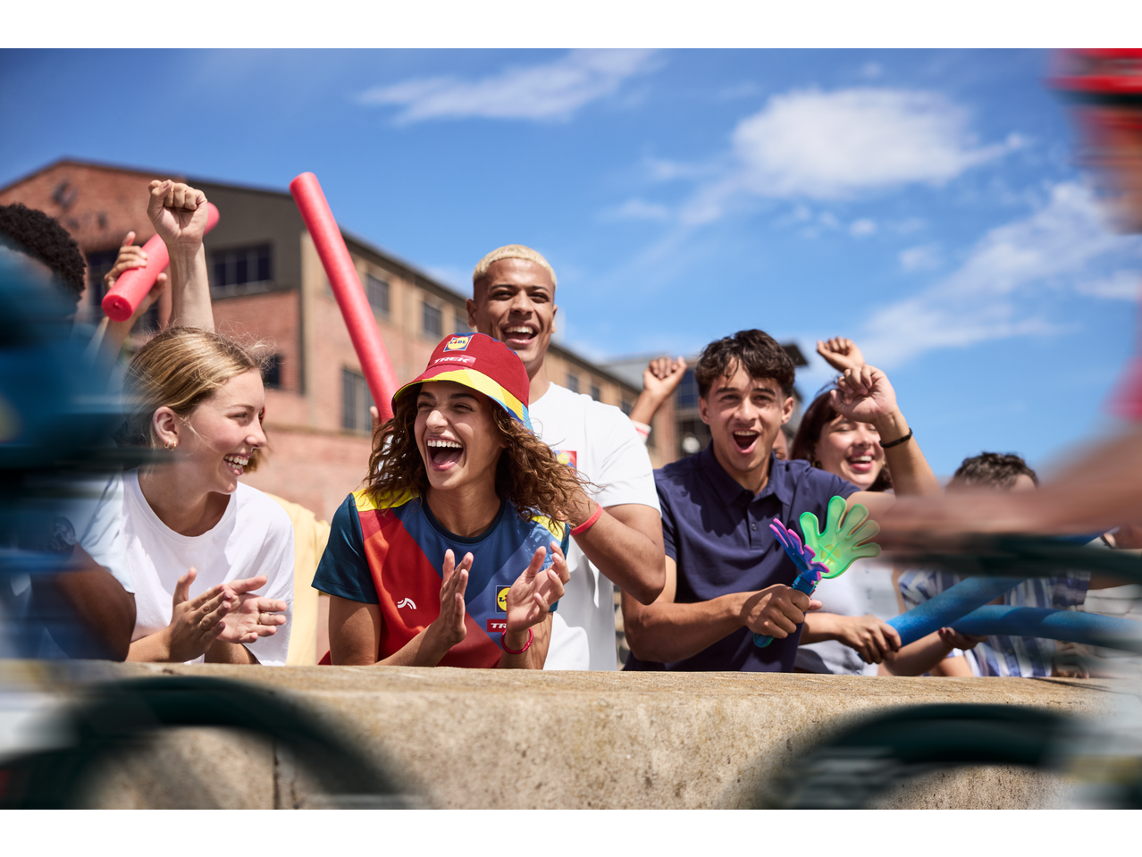 Tineri aplaudând în tricouri funcționale CRIVIT și pălării tip pescar Lidl Trek.