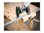 A cordless drill being used to drill a hole in a metal bar on a wooden workbench.