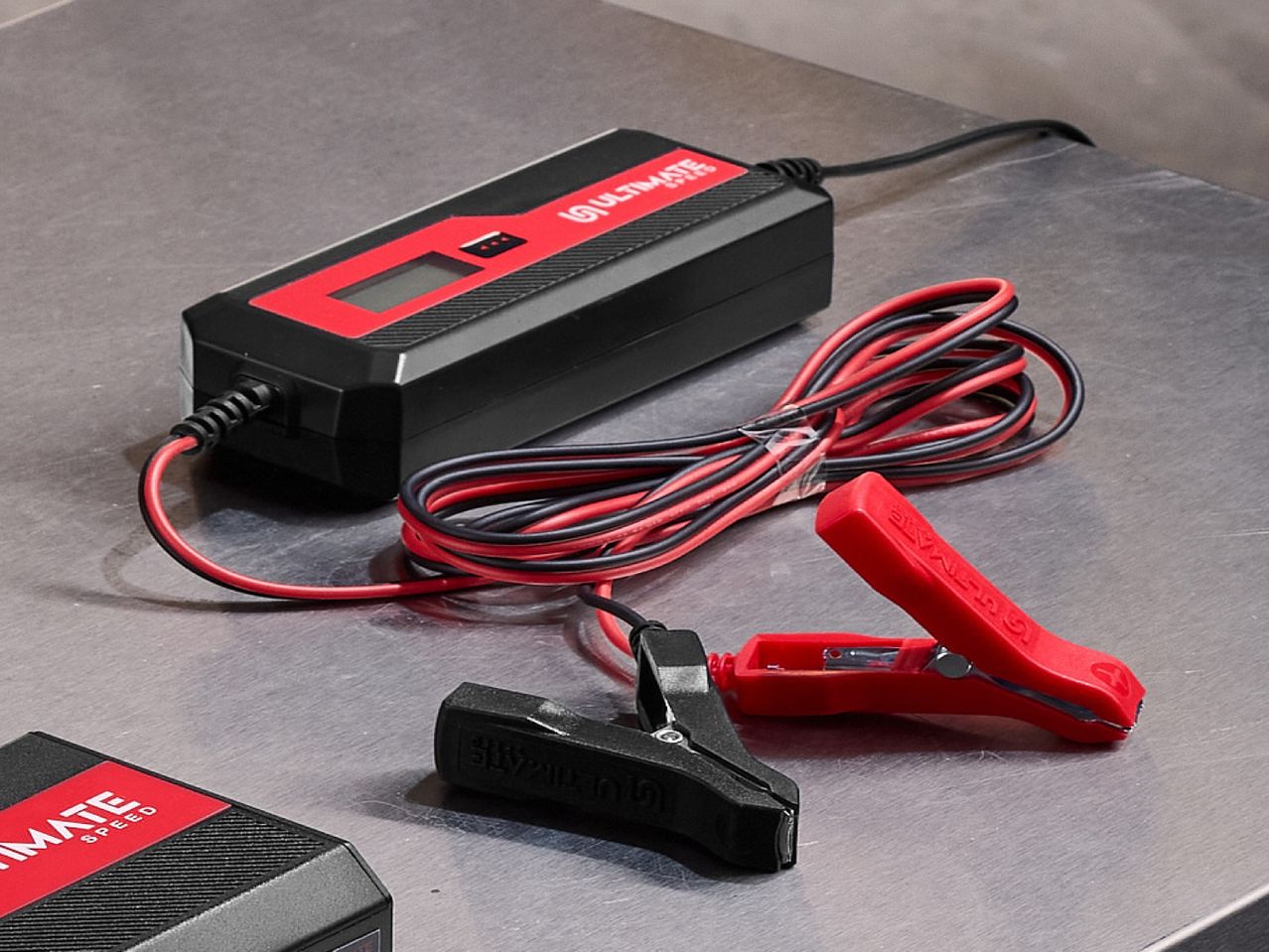 A black and red car battery charger with jumper cables on a metallic surface.