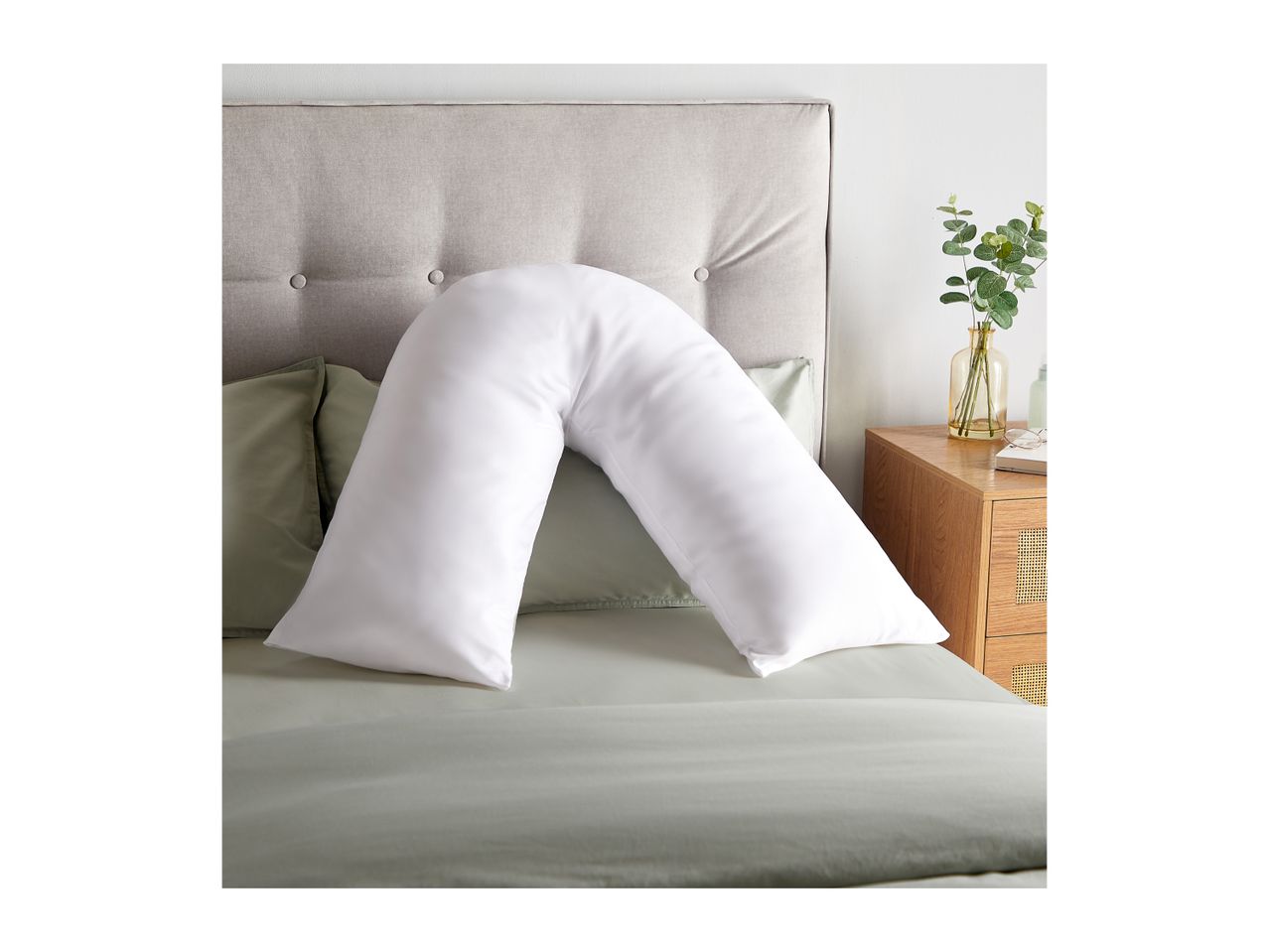 White V-shaped pillow on a bed with a grey headboard and green bedding.