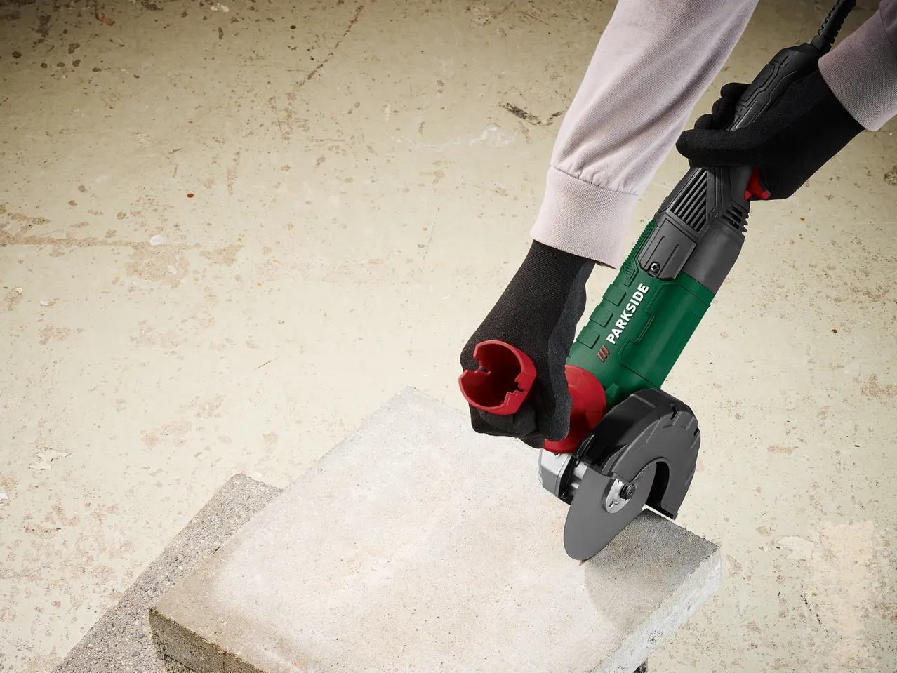 Човек с ръкавици използва ъглошлайф Parkside, за да реже бетонна плоча.
