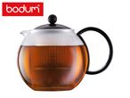 Glass teapot with black lid and handle, filled with amber tea, on a white background.