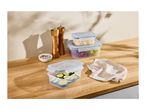 Food storage containers with grapes, cheese, and zucchini on a wooden counter with spices.