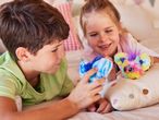 Two children playing with colorful, fluffy toys on a bed.