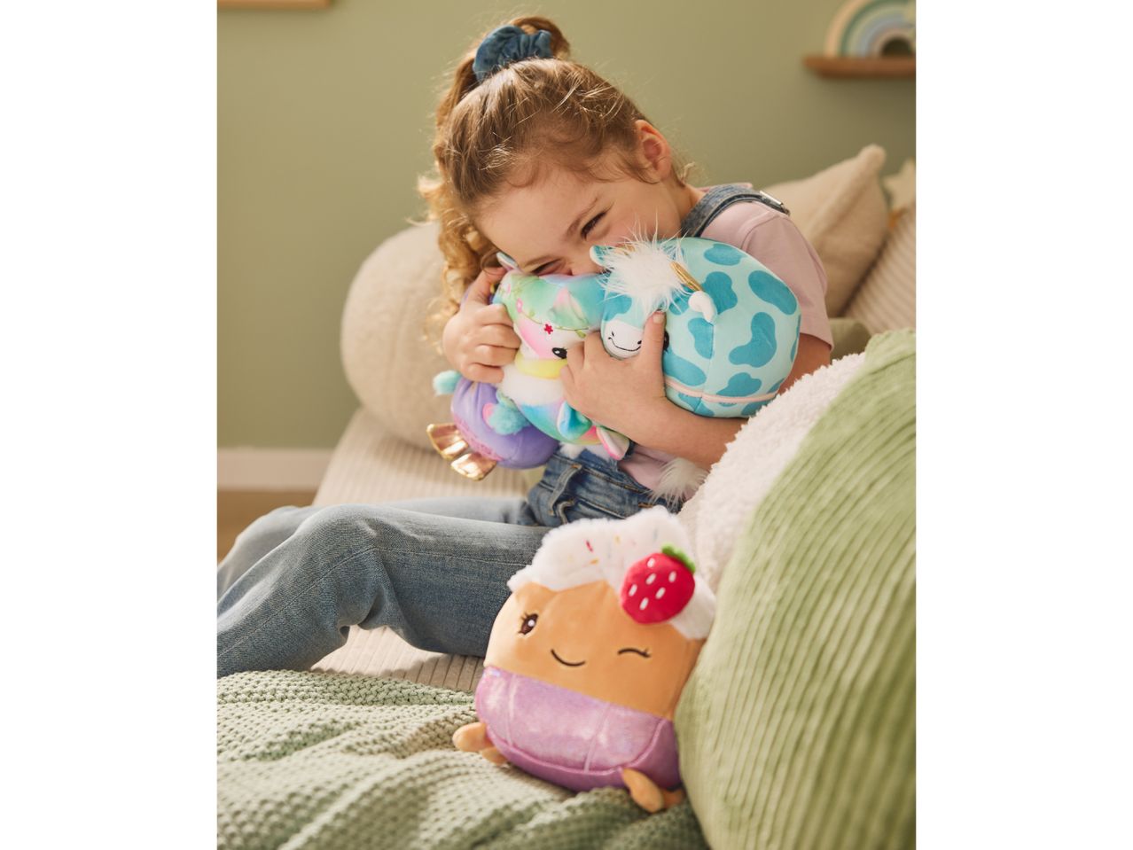 A young girl hugging two plush toys, with a cupcake plush toy in the foreground.