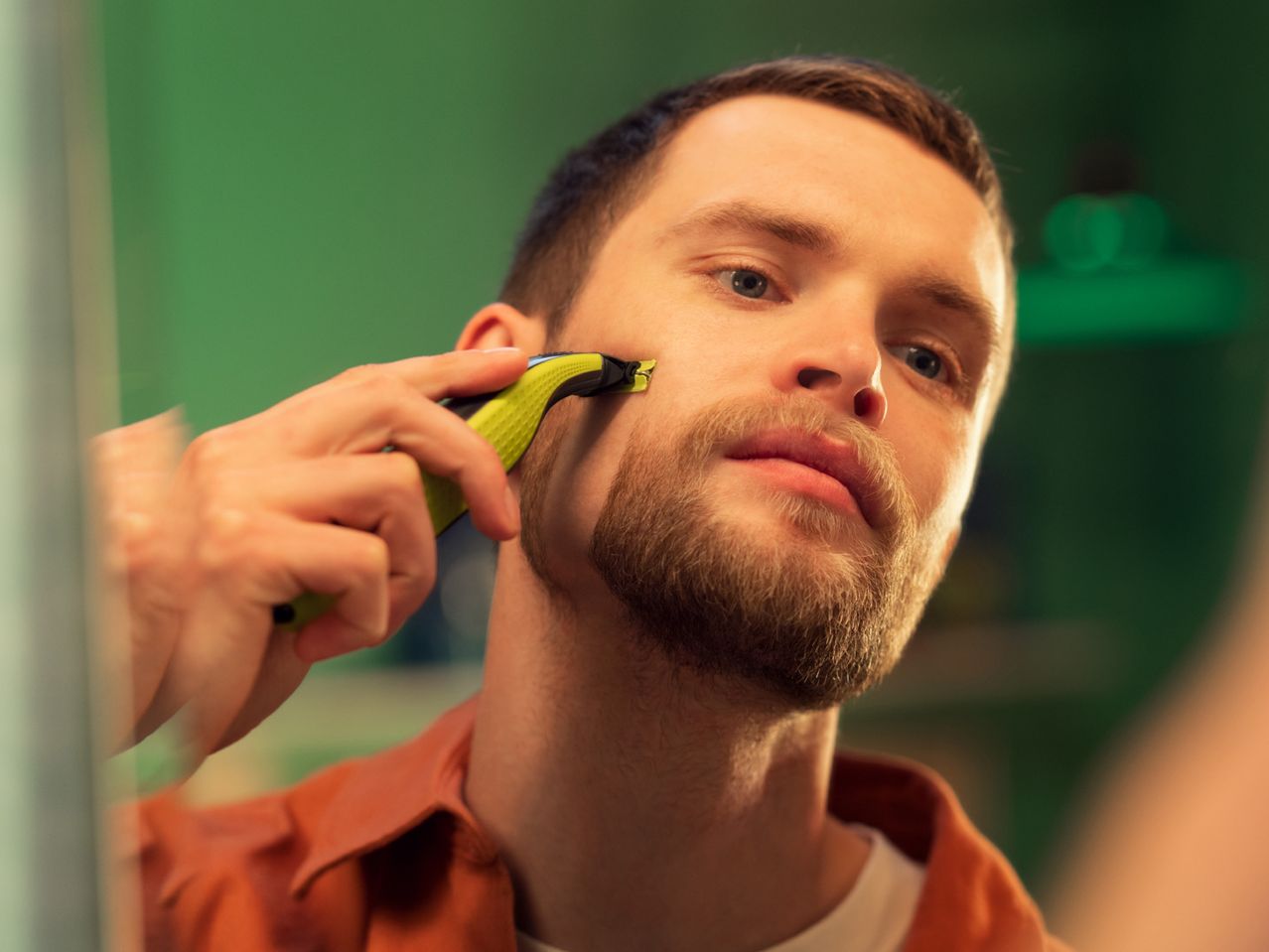 Man trimming his beard with an electric shaver in front of a mirror
