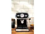 Máquina de café preta com medidor de temperatura e chávenas numa bancada de madeira.