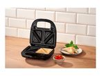 Open sandwich maker with toasted sandwiches, fresh basil, and cherry tomatoes on a wooden counter.