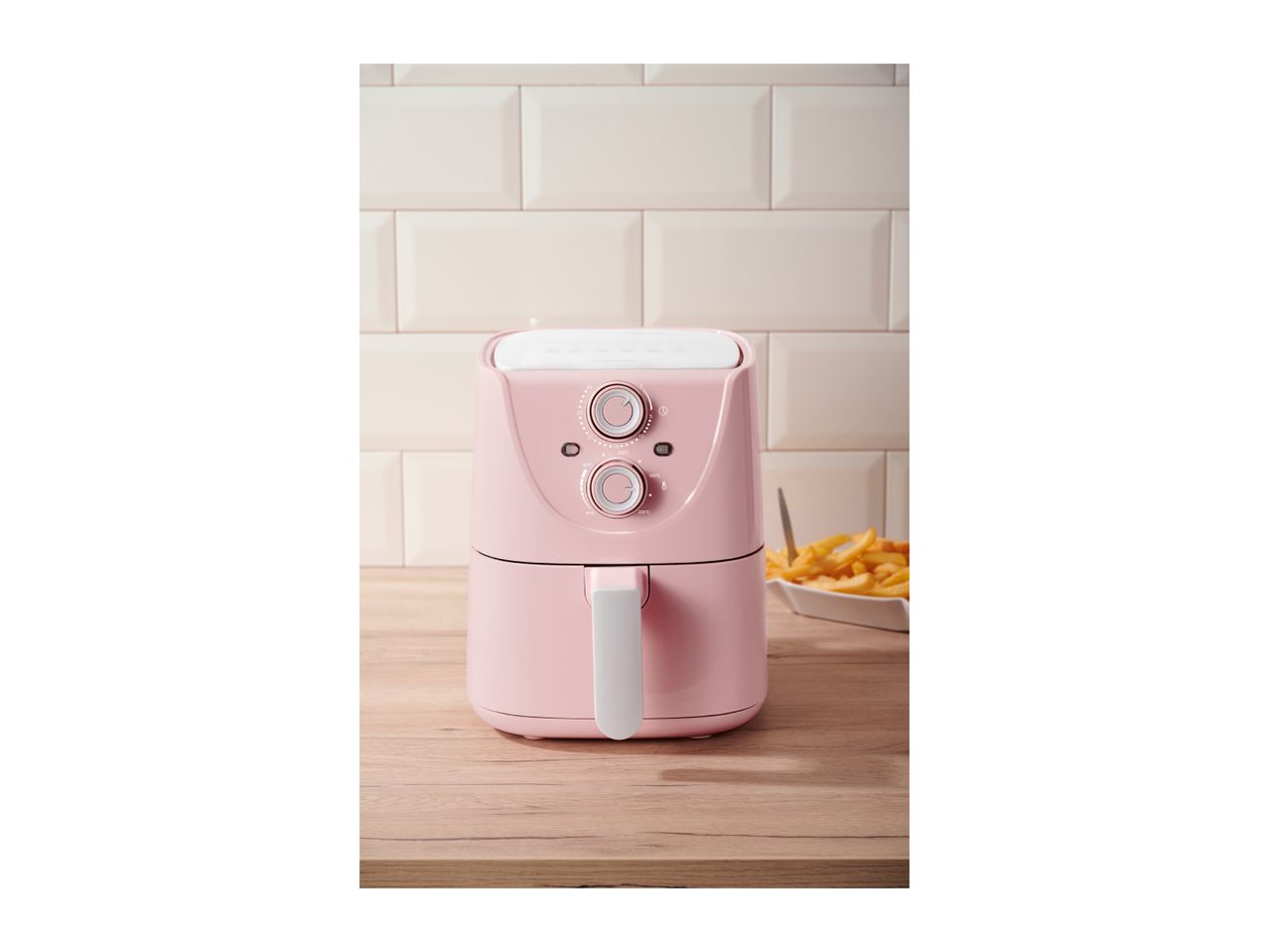 A pink air fryer on a wooden counter with a bowl of french fries.