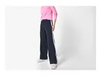A person wearing pink long-sleeved top, black wide-leg trousers with white stripes, and sneakers