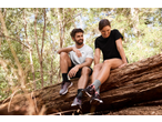 Homem e mulher com t-shirts CRIVIT sentados num tronco na floresta.