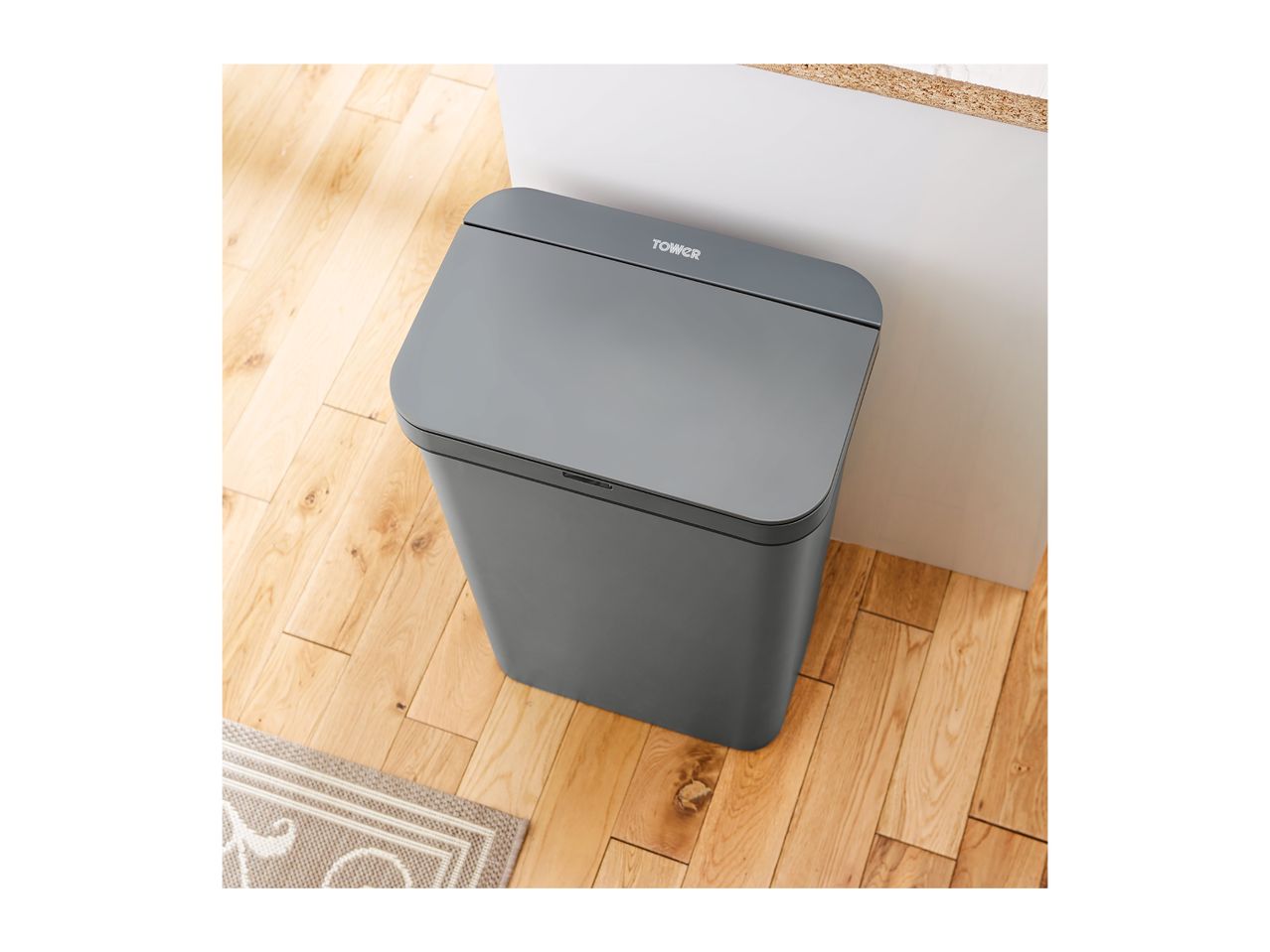 A grey Tower brand step bin sits on a light wood floor.