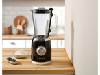 A black and silver blender on a wooden counter with blueberries and cream.