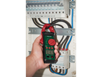 Mão segurando um amperímetro de pinça digital Parkside medindo corrente em um quadro elétrico Hager.