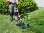 Férfi akkumulátoros fűnyíróval vágja a füvet a kertben.