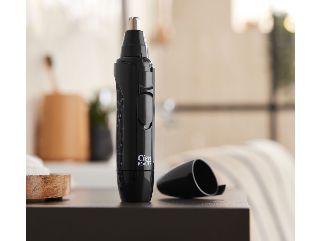 A black nose and ear hair trimmer sits on a counter next to its protective cap.