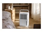 A white portable dehumidifier with a carrying handle on a wooden floor in a bedroom.