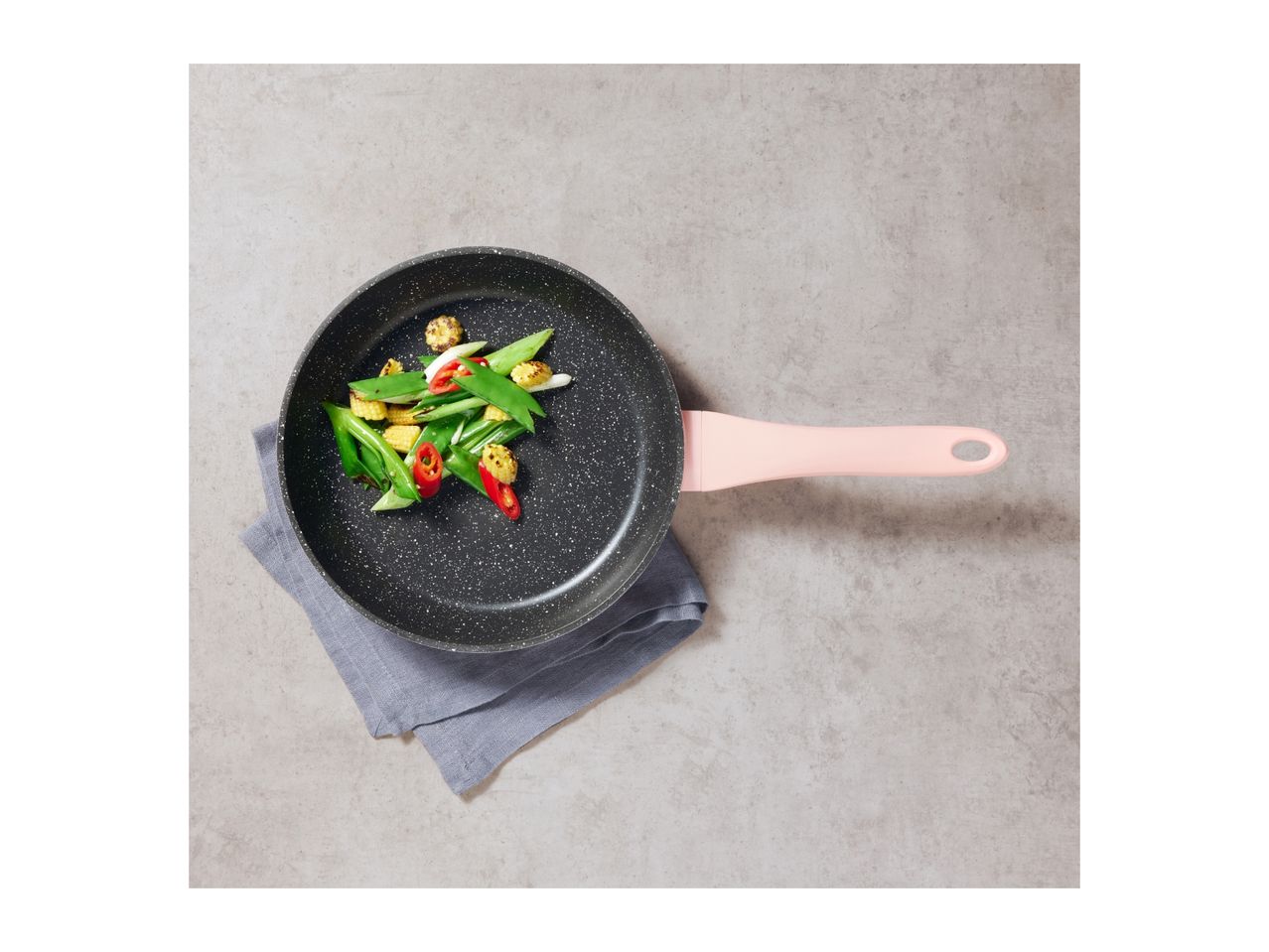 A black speckled frying pan with a pink handle, holding stir-fried vegetables.