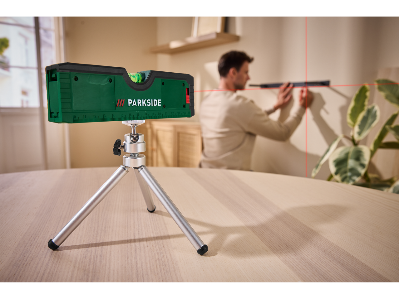 Parkside lazerinis nivelyras ant trikojo, projektuojantis raudonus kryžius ant sienos.