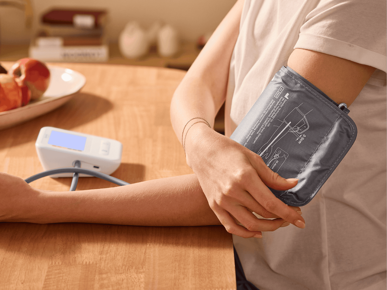Person misst Blutdruck mit einem Blutdruckmessgerät auf einem Holztisch.