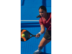 Mulher a jogar padel com raquete e bola num campo azul.