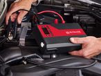 A person connecting a portable jump starter to a car battery.