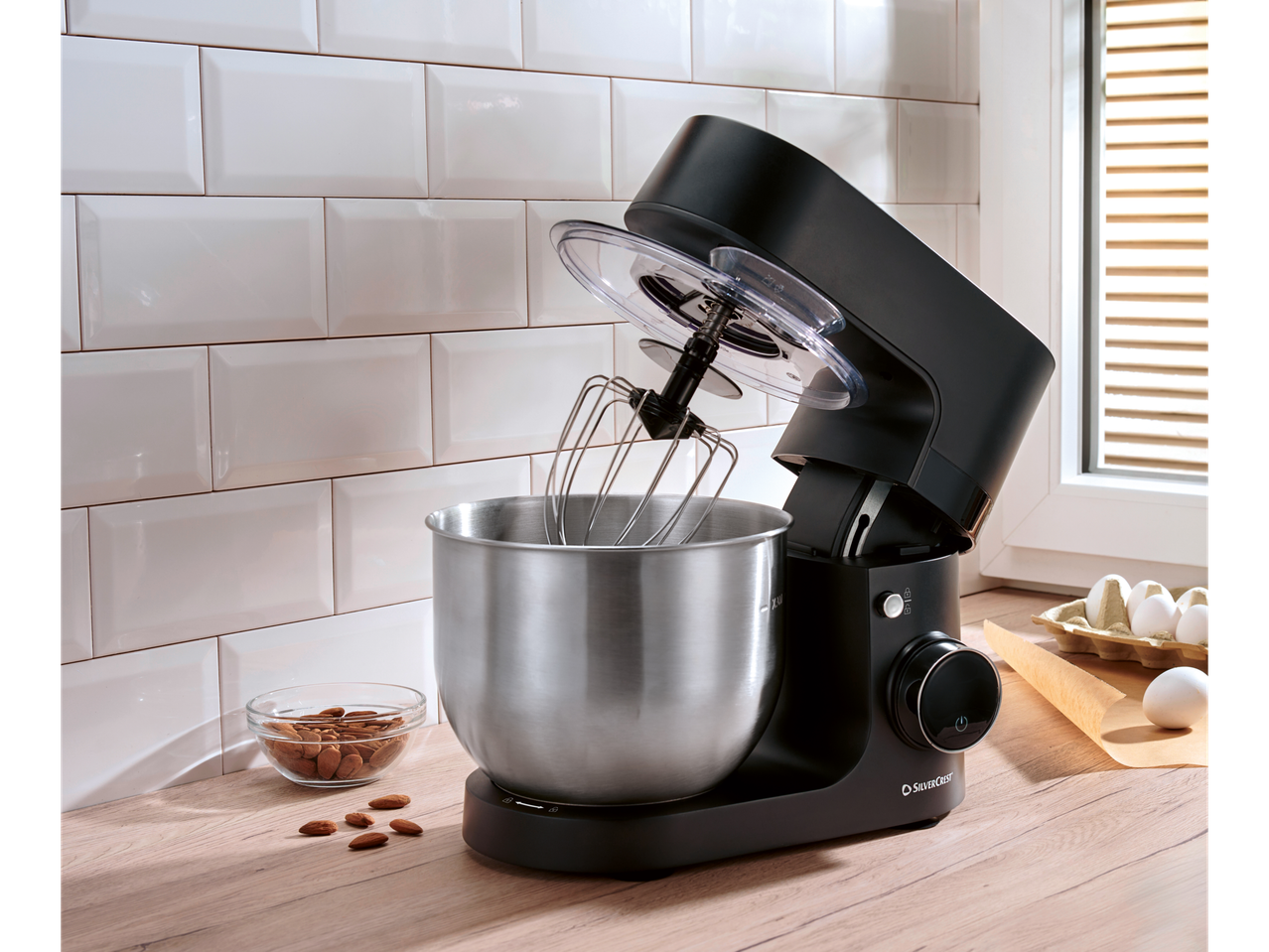 Black SILVERCREST® stand mixer with a stainless steel bowl, whisk, almonds, and eggs.
