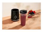 A personal blender base next to a cup filled with a berry smoothie on a wooden table.