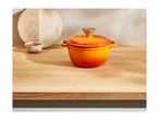 An orange cast iron pot with a lid on a wooden countertop next to a cutting board.