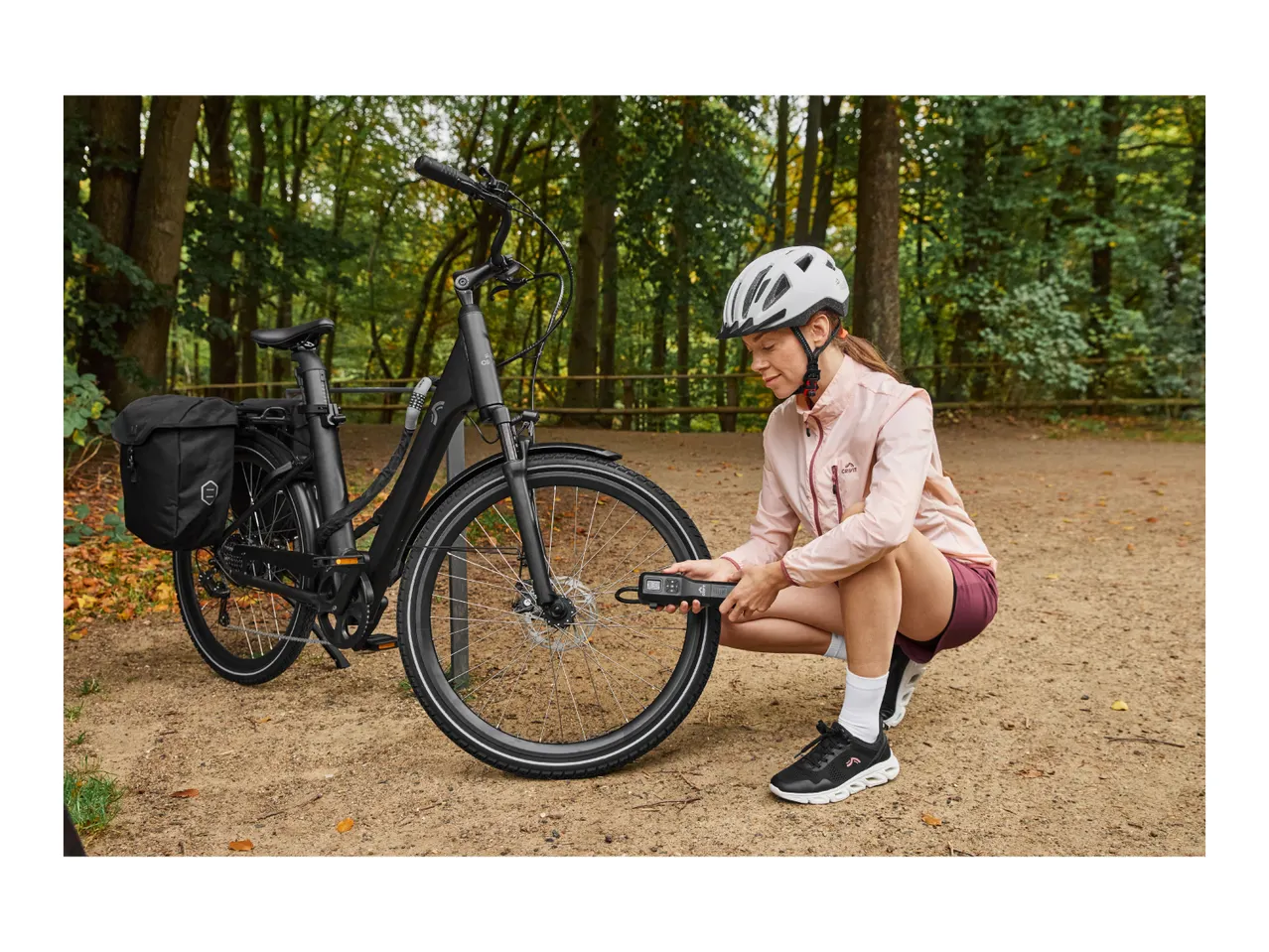 Woman in a helmet inflating a bicycle tire with a portable pump in a park.
