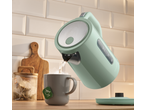 Chaleira verde clara a verter água quente para uma caneca cinzenta com um saco de chá.