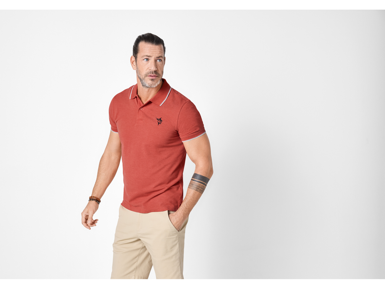 Bărbat în tricou polo roșu și pantaloni bej, cu un tatuaj pe braț.