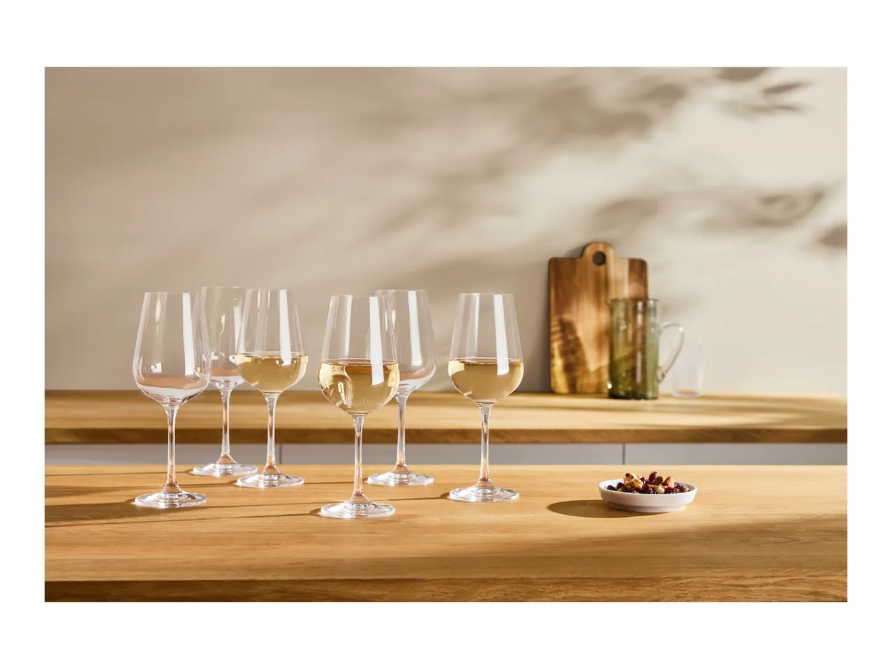 White wine glasses, some filled, on a wooden counter with a bowl of nuts.