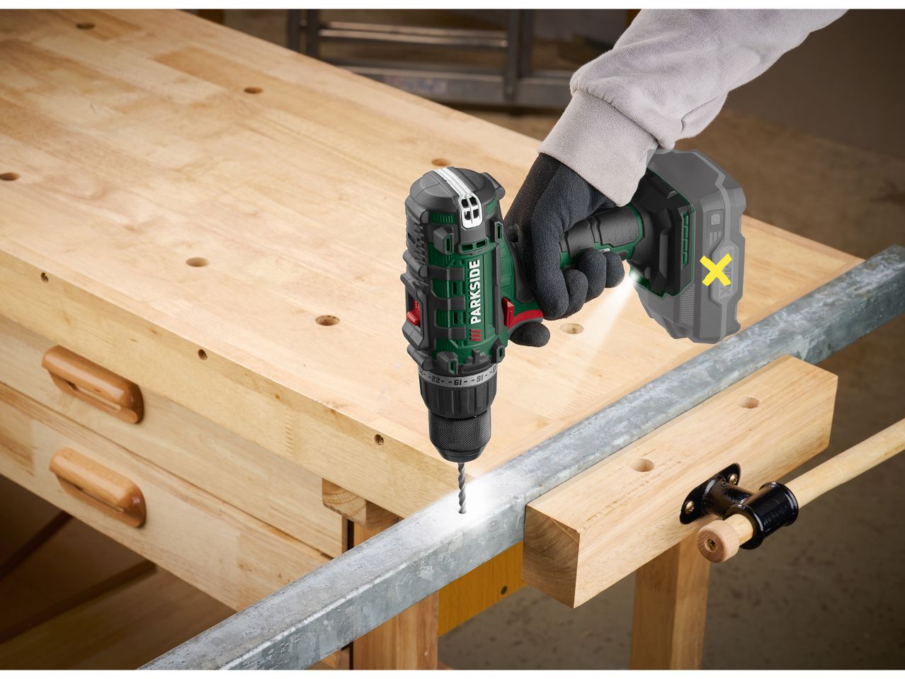 A person uses a Parkside cordless drill driver to drill into a metal bar on a workbench.