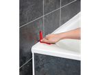 Uma mão usa uma ferramenta vermelha de selante de silicone para aplicar selante em um banheiro.