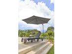 Espreguiçadeira de jardim com almofadas cinzentas e grande guarda-sol num terraço ensolarado.