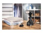 Handheld garment steamer with folded clothes on a wooden table.