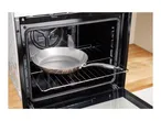 Open oven with a frying pan on the rack, showing the interior and wooden countertop.