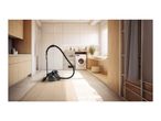 A black canister vacuum cleaner on a rug in a modern, bright laundry room.