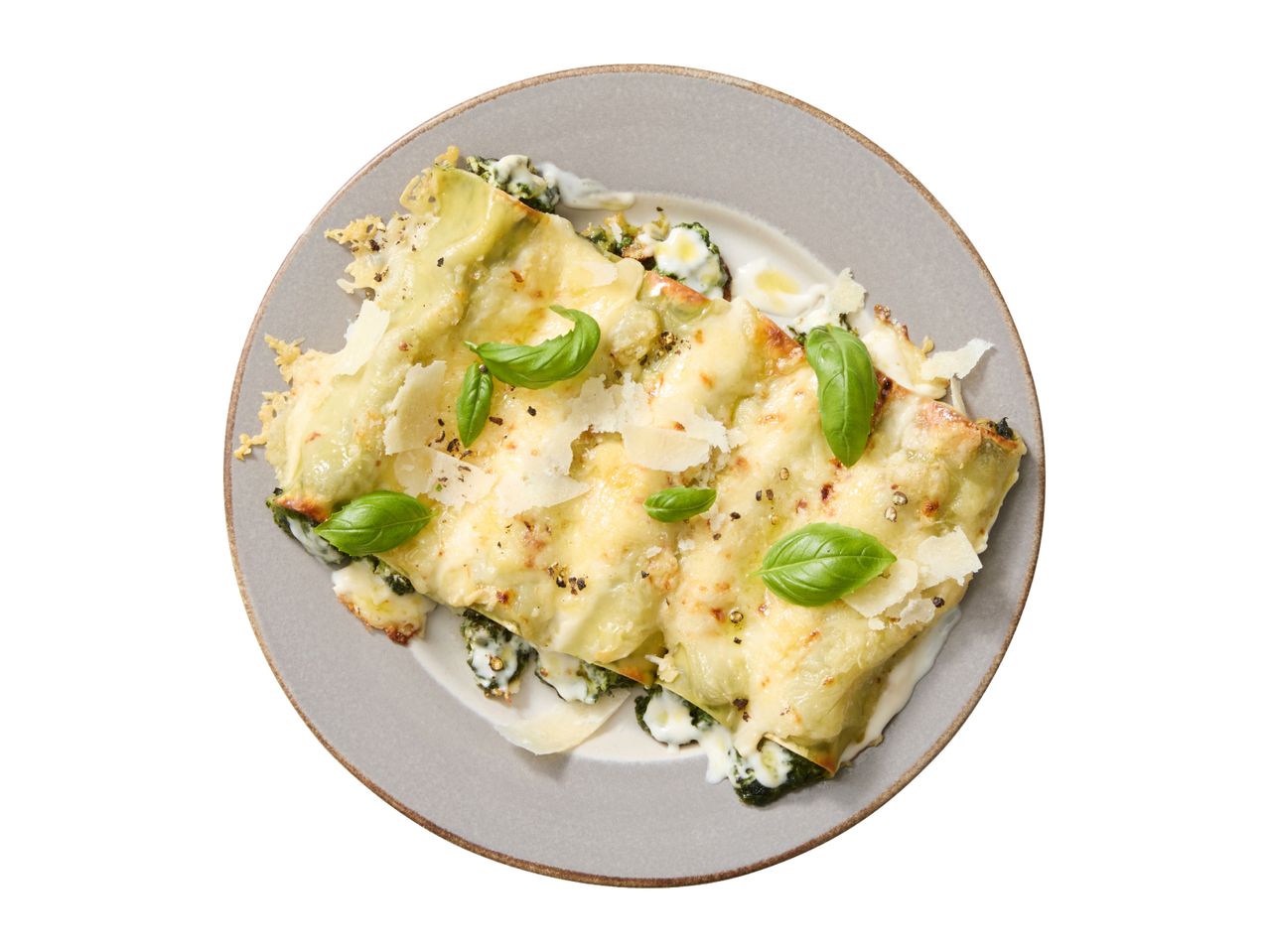 Overhead shot of cannelloni with spinach and ricotta, topped with cheese, basil, and pepper.
