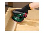 A person wearing a black glove uses a green and black cordless sander on a wooden surface.