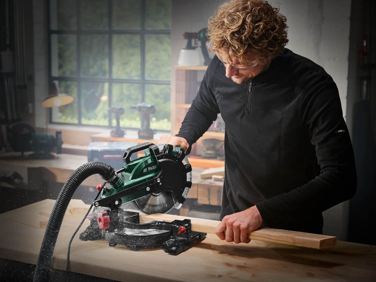 A man using a Parkside miter saw to cut wood in a workshop.