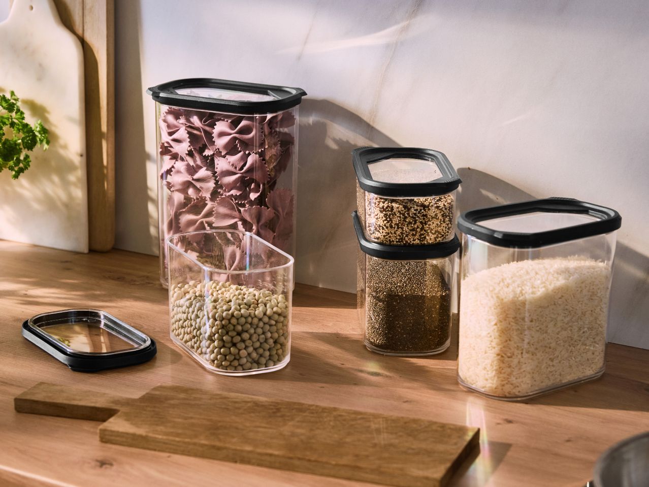 Clear food storage containers with various dry goods like pasta, lentils, quinoa, chia seeds, and rice.