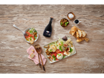 Een fles balsamicoazijn van Italiamo omringd door een salade, brood en een kaasplank.