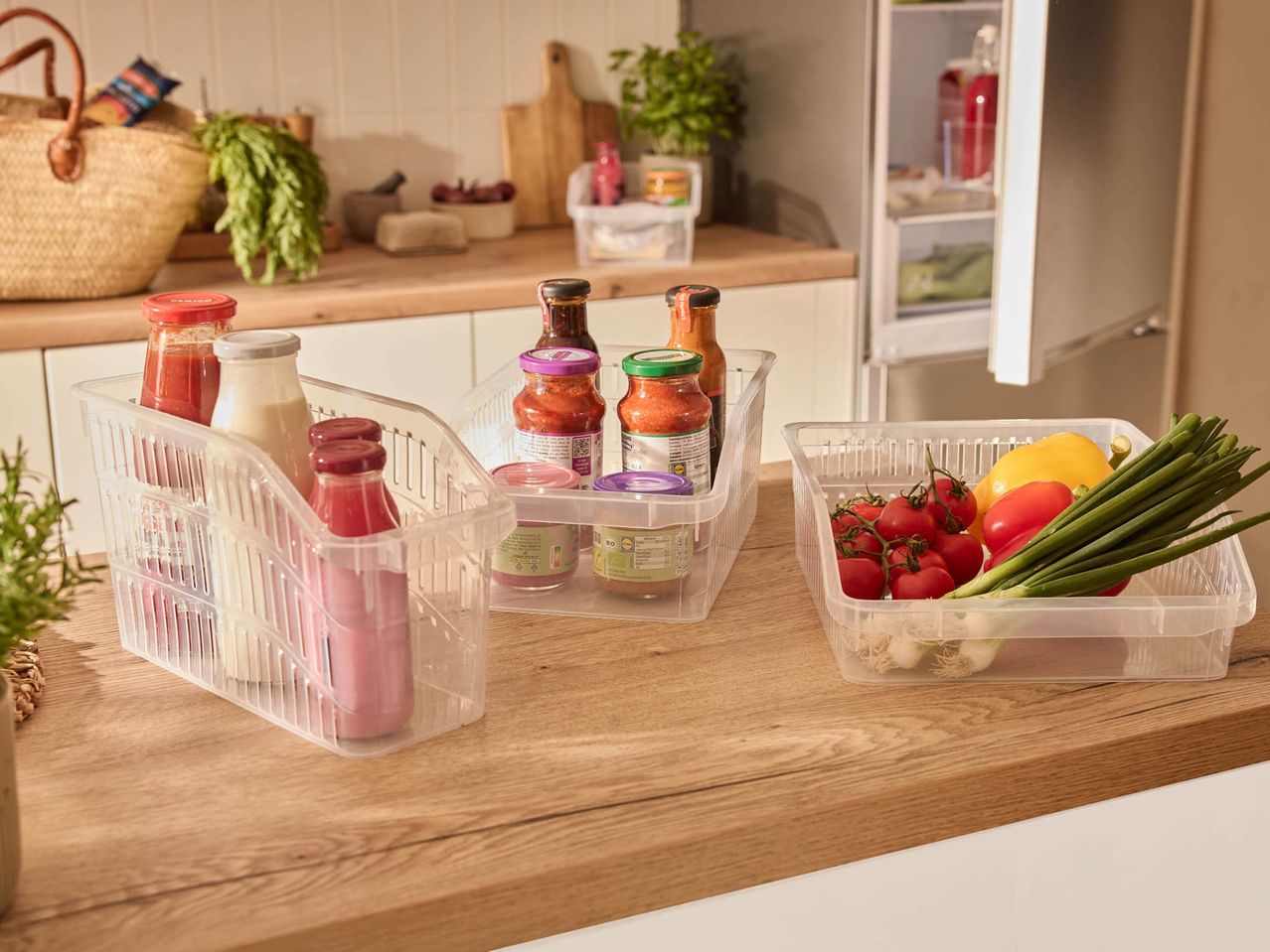Clear plastic organizers on a kitchen counter, holding sauces, drinks, and fresh produce.