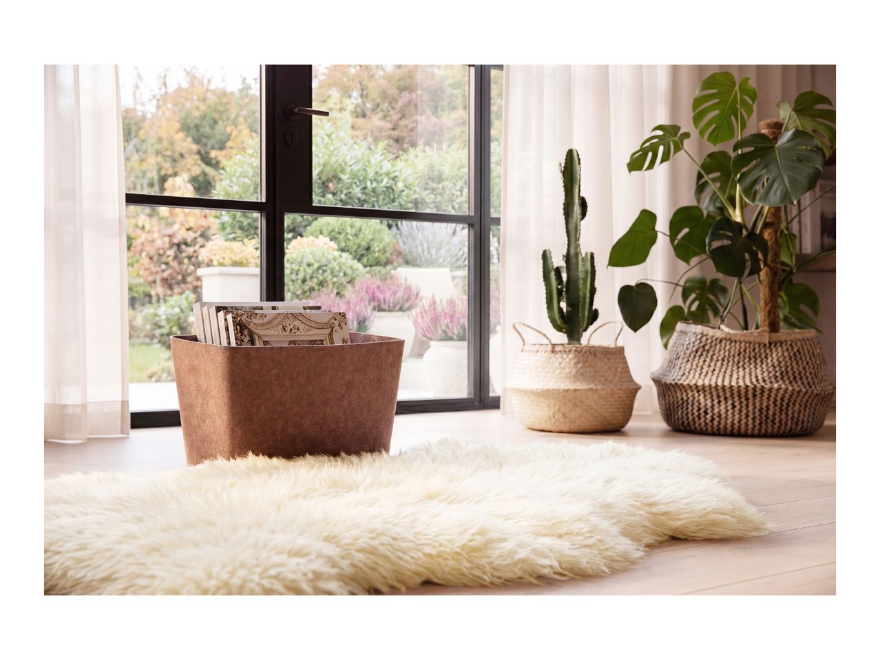 A fluffy white sheepskin rug on a wooden floor next to plants and a storage basket.