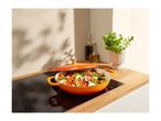 Orange Le Creuset Dutch oven with vegetables on an induction cooktop.
