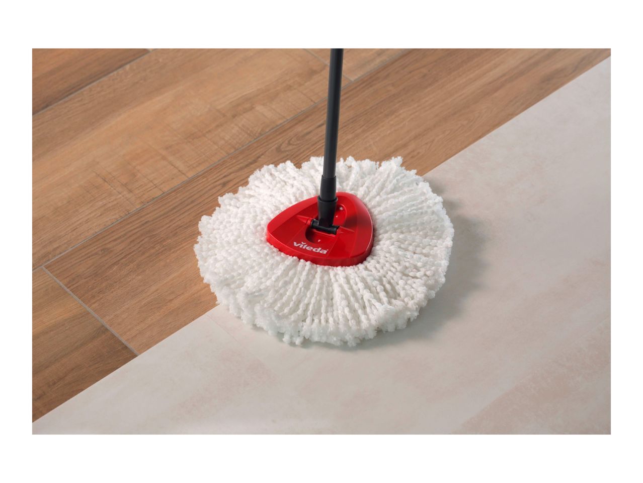 A Vileda mop with a fluffy white head cleans a light-colored floor.